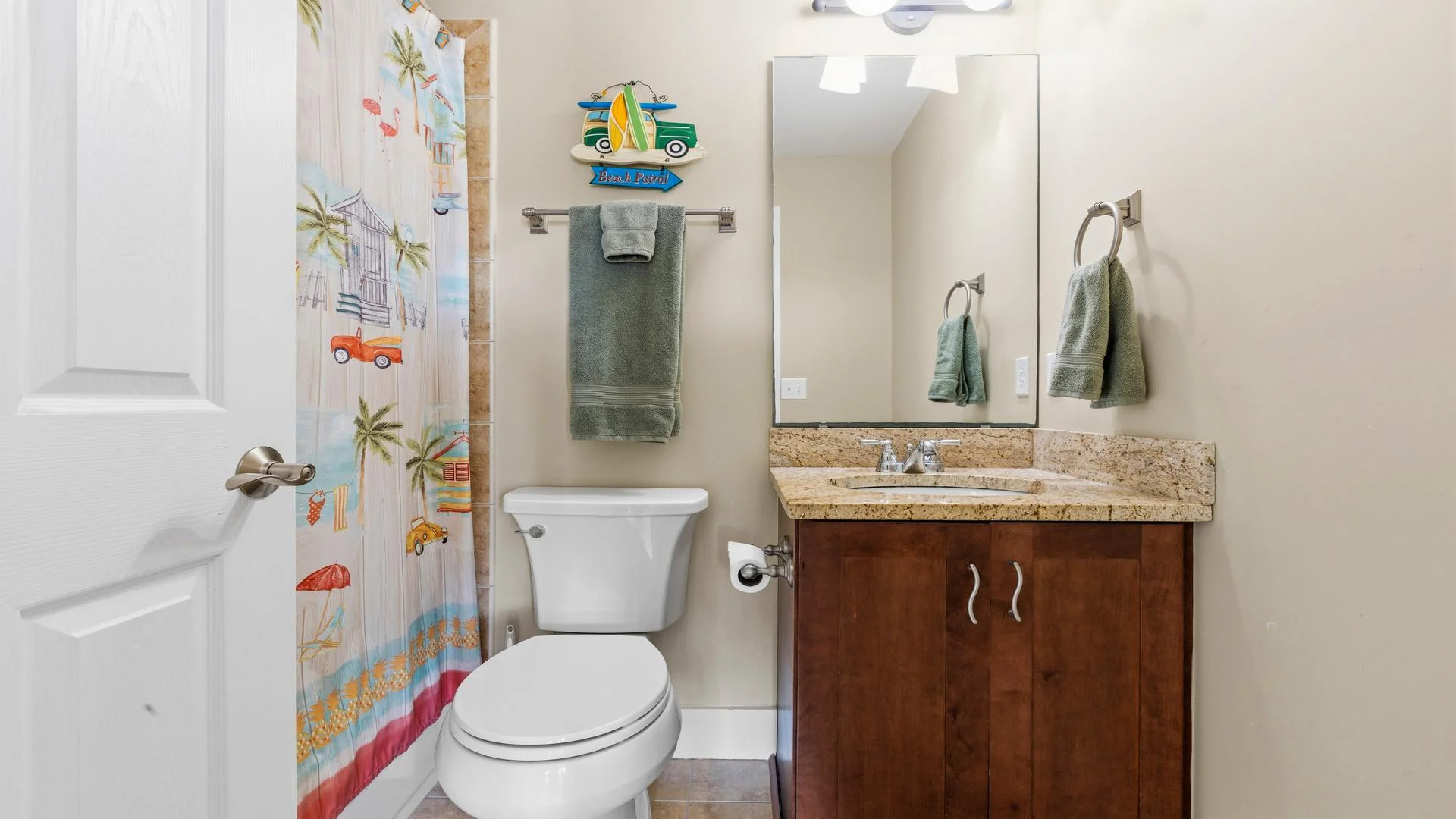 Bathroom with brown granite countertop, wood vanity, white toilet, and colorful beach-themed shower curtain.