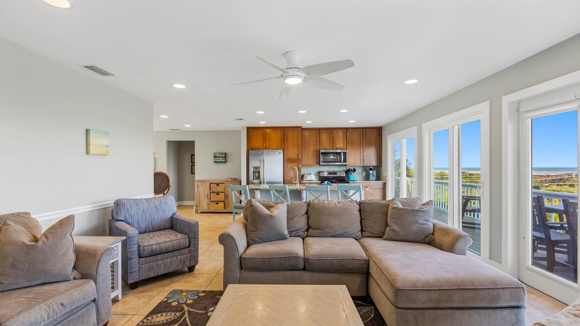 Living area with gray sectional and armchair, a tiled floor, and ocean views through sliding glass doors.