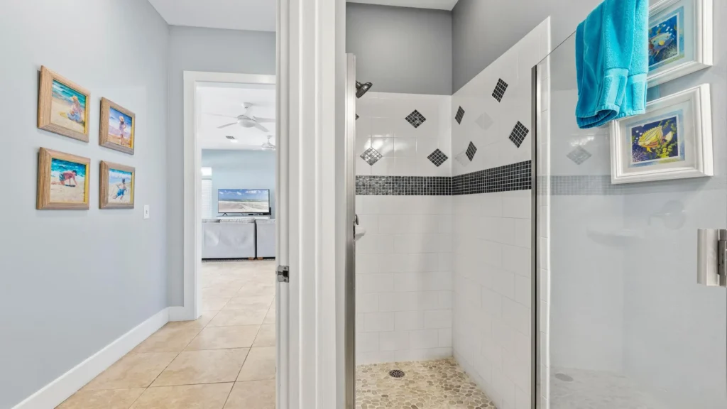 Shower features white tiles with black mosaic accents and a pebble stone floor in the bathroom.