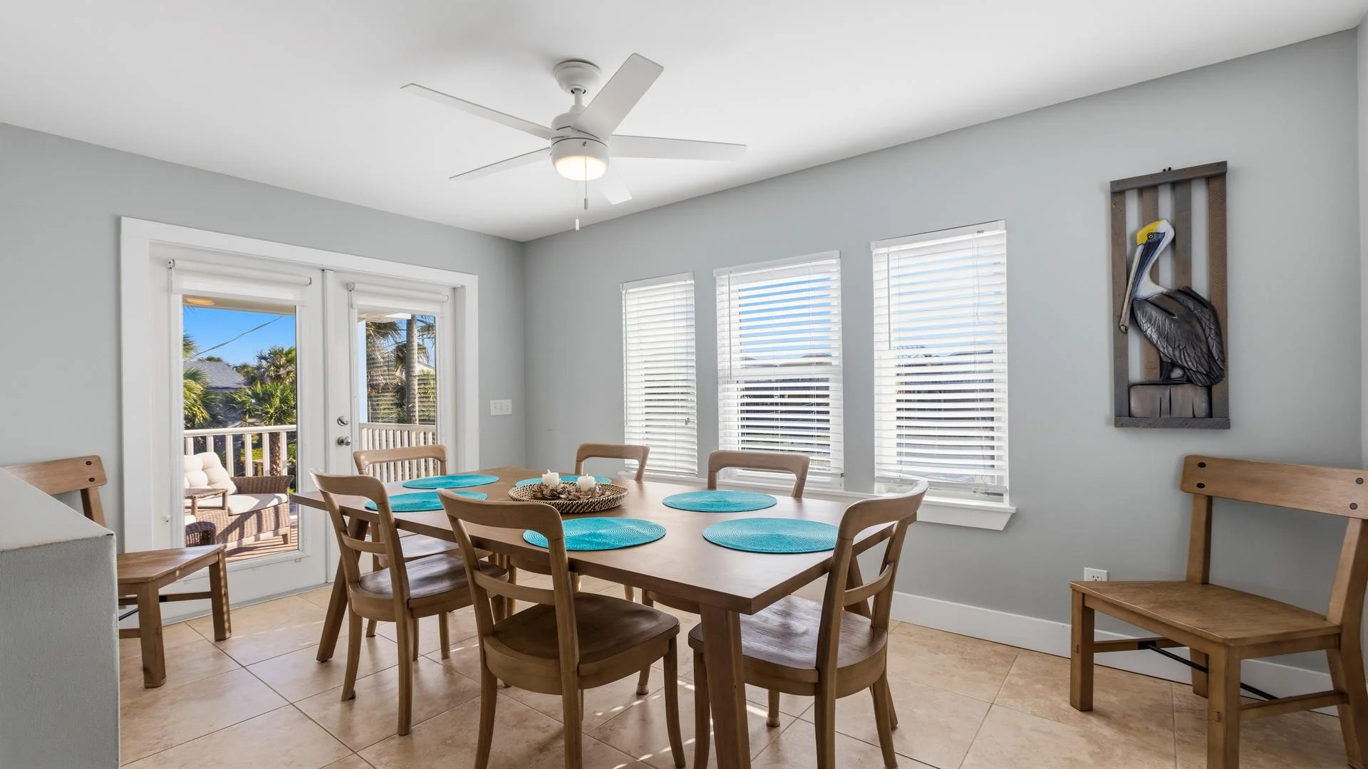 Dining area features a light wood table with six matching chairs and turquoise placemats under a ceiling fan.