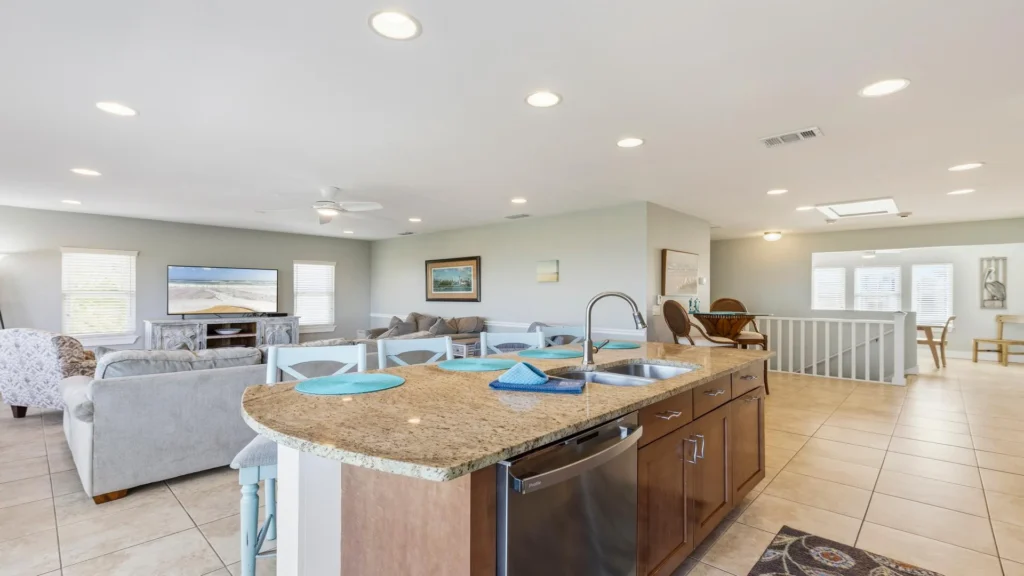 Granite countertop kitchen island with stainless steel sink and dishwasher overlooks the tiled floor living area.