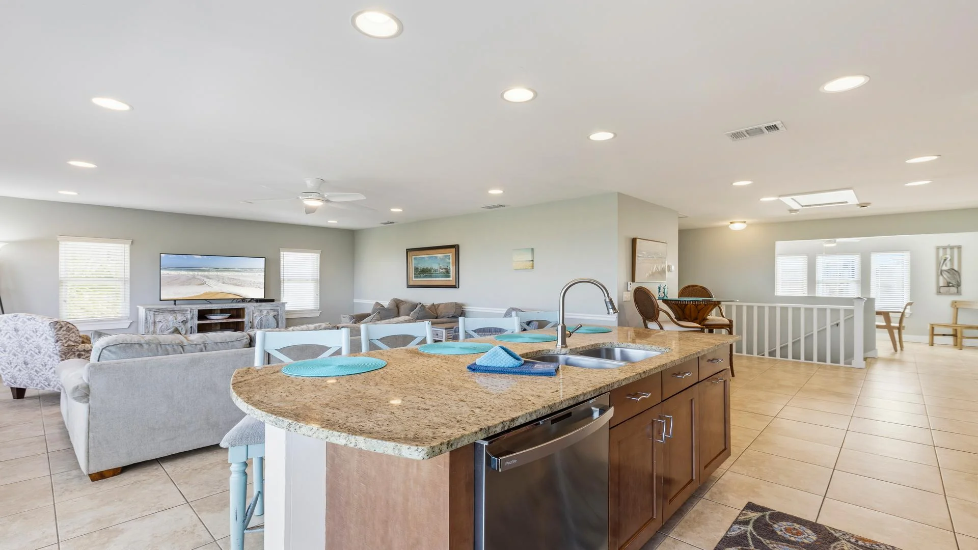 Granite countertop kitchen island with stainless steel sink and dishwasher overlooks the tiled floor living area.