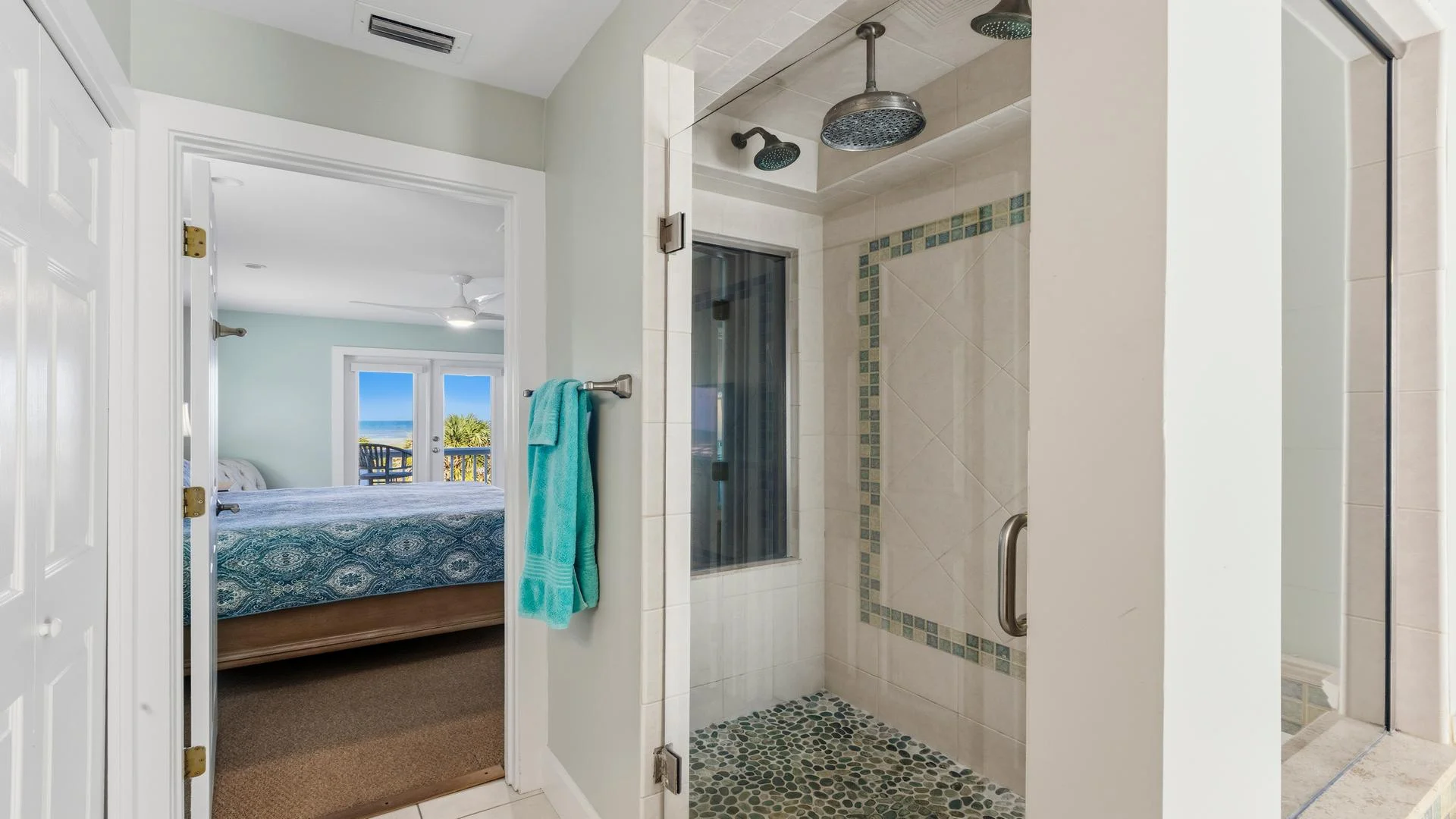 Glass-enclosed shower features pebble stone flooring and tiled walls with blue mosaic border accents.