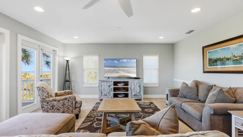 Living room with patterned armchair, gray sofas, a floral rug, and ocean views through glass doors.
