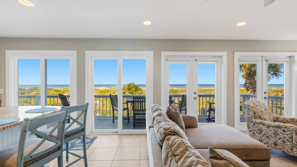 Oceanfront living area features large sliding glass doors opening to a balcony with outdoor seating and beach views.