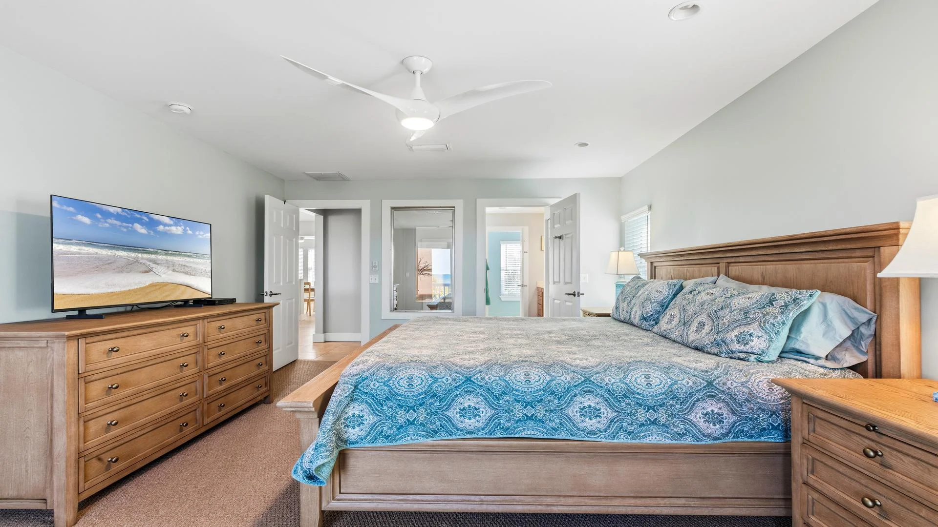 King-size bed with patterned blue bedding faces a wooden dresser topped by a flat-screen TV in the bedroom.