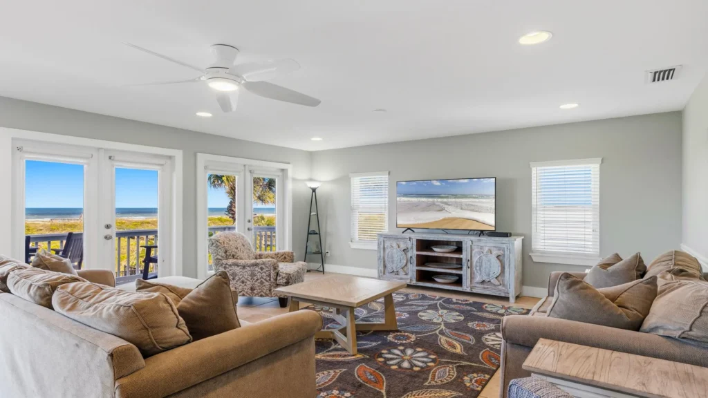 Spacious living room with beige sofas, patterned armchair, wood coffee table, and ocean views through glass doors.