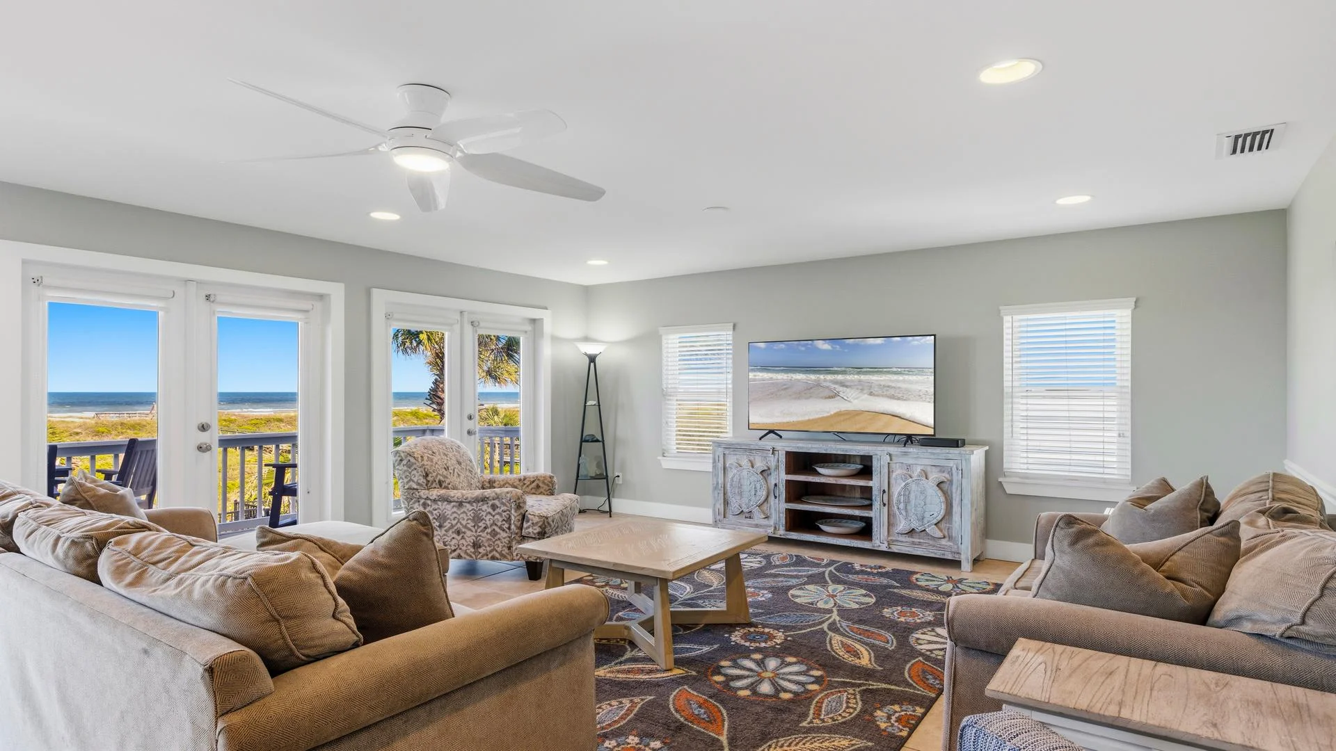 Spacious living room with beige sofas, patterned armchair, wood coffee table, and ocean views through glass doors.