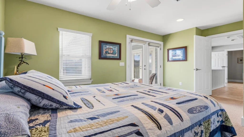 Quilted bedspread with sailboat patterns covers the bed, framed by light green walls and two framed prints.