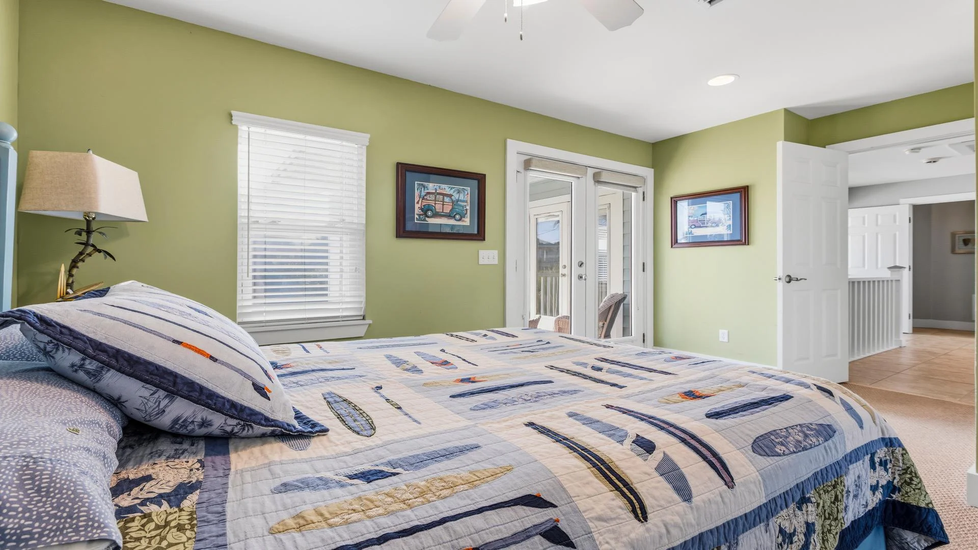 Quilted bedspread with sailboat patterns covers the bed, framed by light green walls and two framed prints.