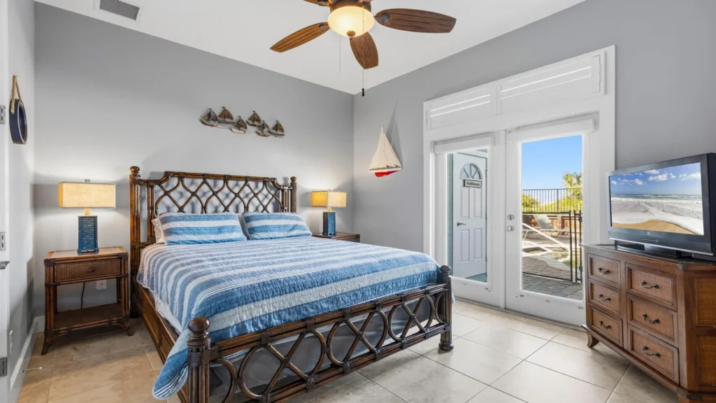First-floor bedroom with a dark wicker dresser topped by a TV and glass doors leading outside.