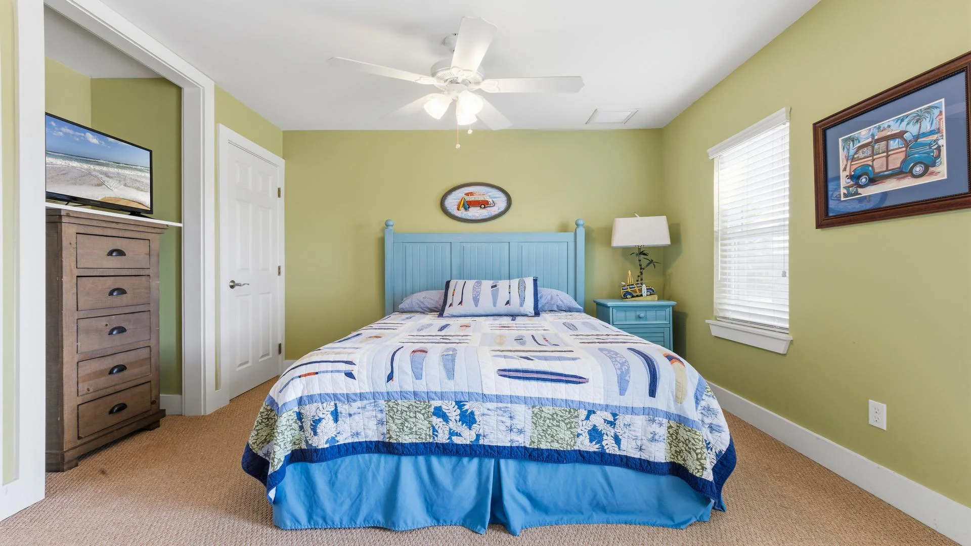 Flat-screen TV sits atop a tall wooden dresser in the corner of the bedroom with green walls and beige carpeting.