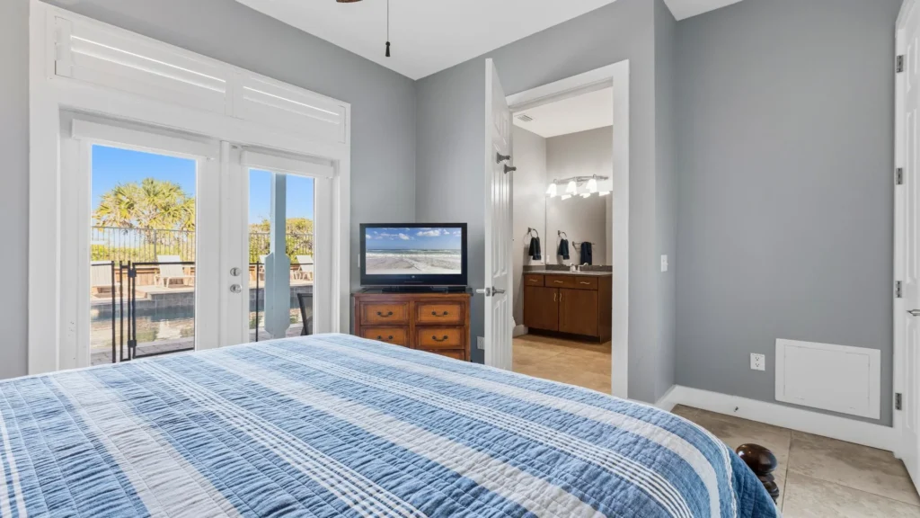 Bedroom with blue plaid bedding, wood dresser holding a TV, and glass doors opening to the pool deck.