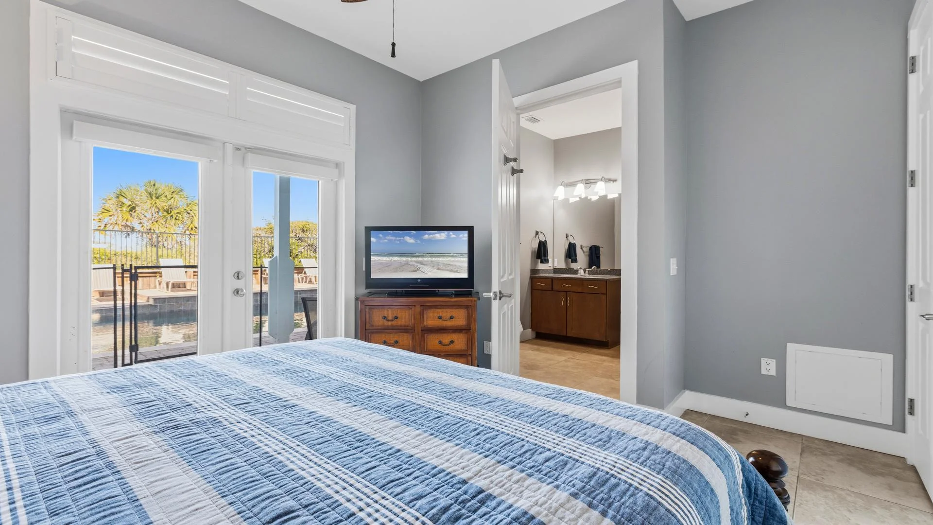 Bedroom with blue plaid bedding, wood dresser holding a TV, and glass doors opening to the pool deck.