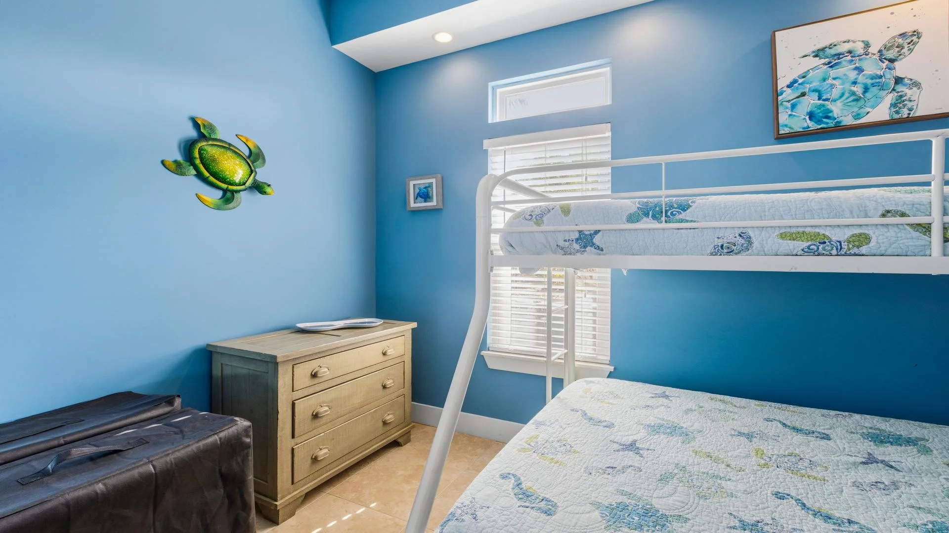 Bunk bedroom with ocean-themed quilts, blue walls, a wooden dresser, and sea turtle wall art.