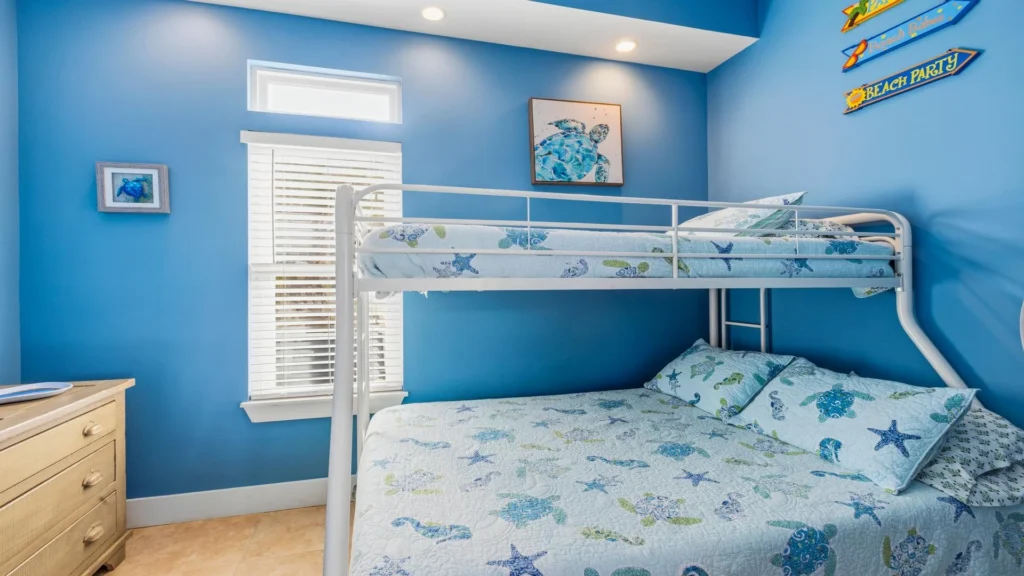 First-floor bunk bed with a white metal frame and a sea-life quilt set against blue walls with coastal artwork.