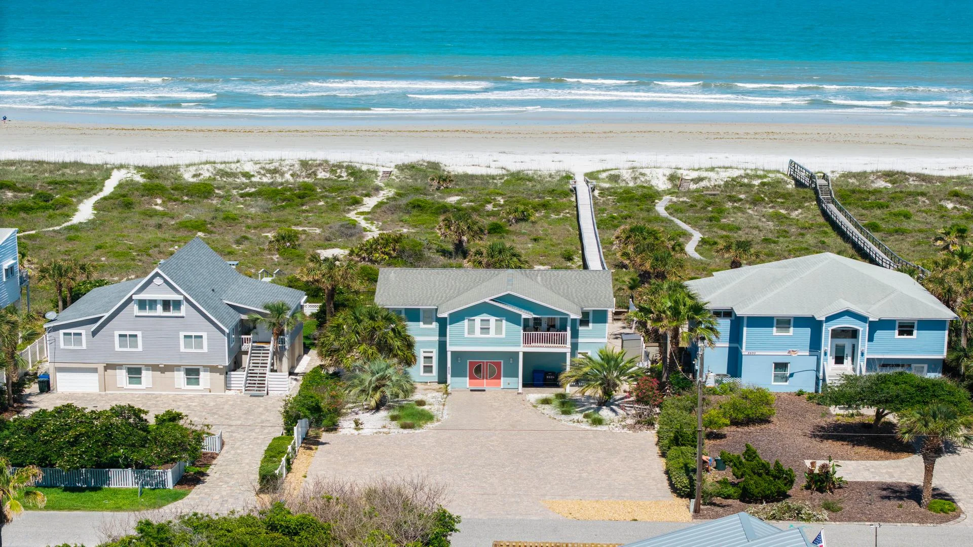 Oceanfront view of three beach houses with direct sandy pathways leading to the shore and turquoise waves beyond.