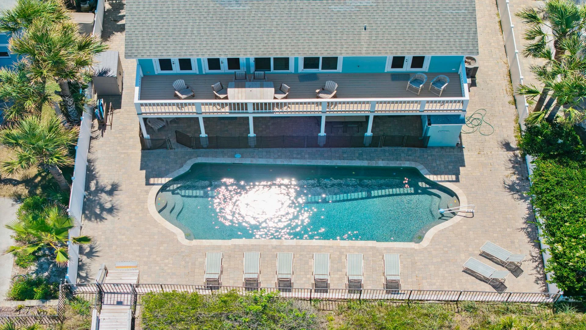 Rectangular pool with curved corners surrounded by stone pavers, lounge chairs, and a shaded second-story deck.