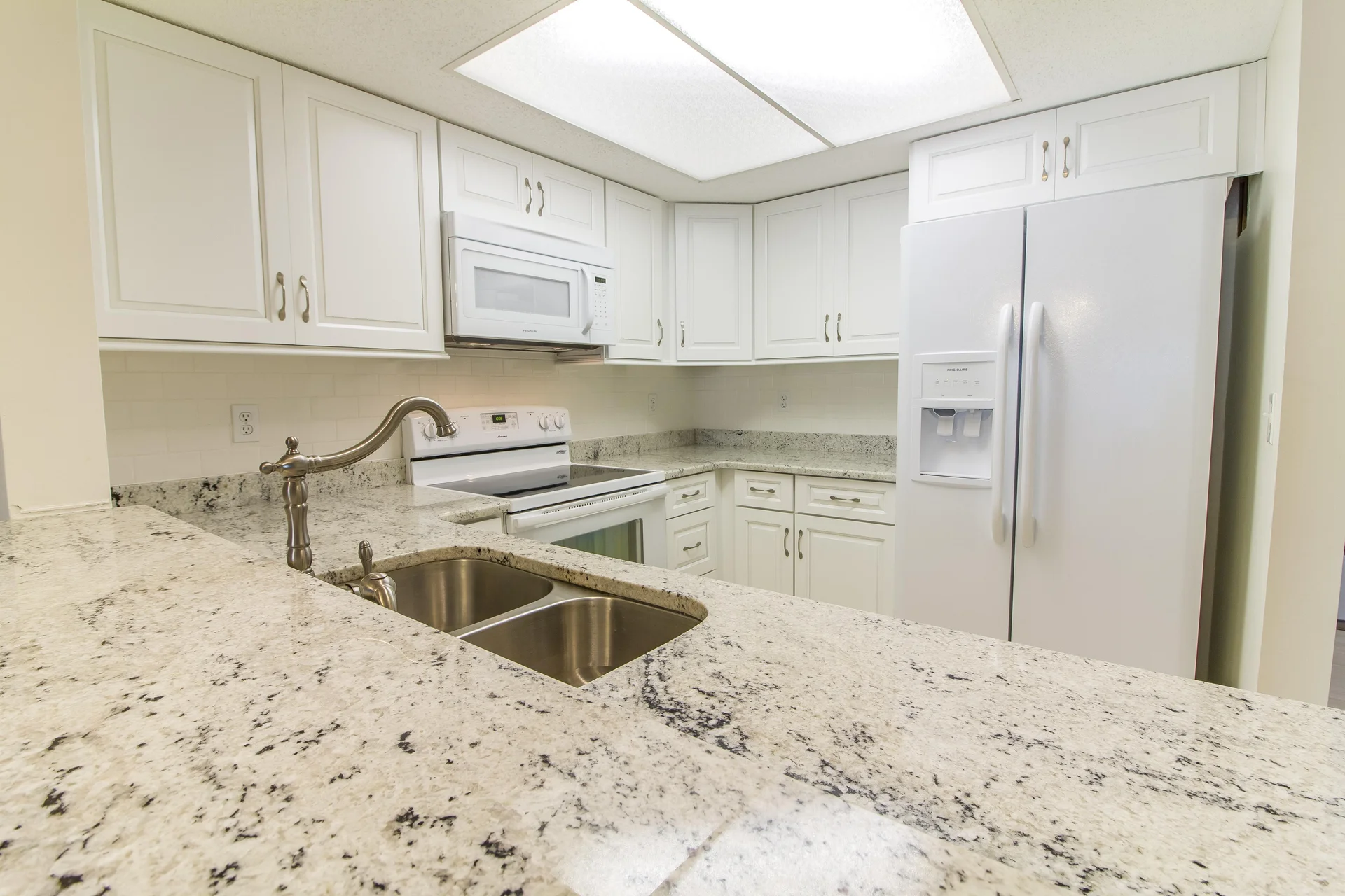 Granite countertops with undermount double sink complement white cabinetry and appliances in the kitchen.