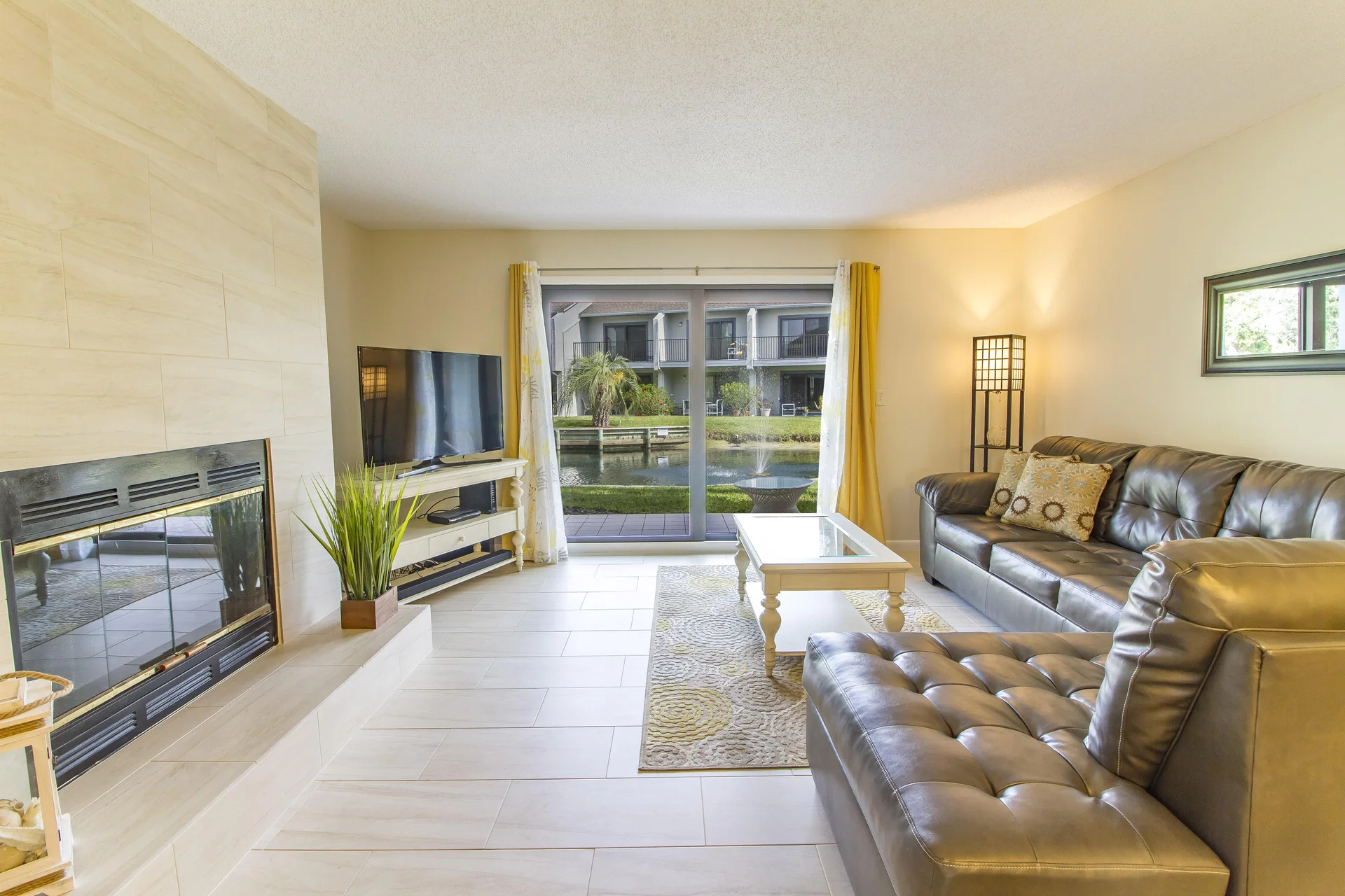 Leather sectional faces a glass-top coffee table and TV, with sliding doors opening to a lagoon view.