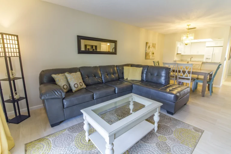 Black leather sectional sofa with patterned pillows faces a white coffee table on a textured area rug.