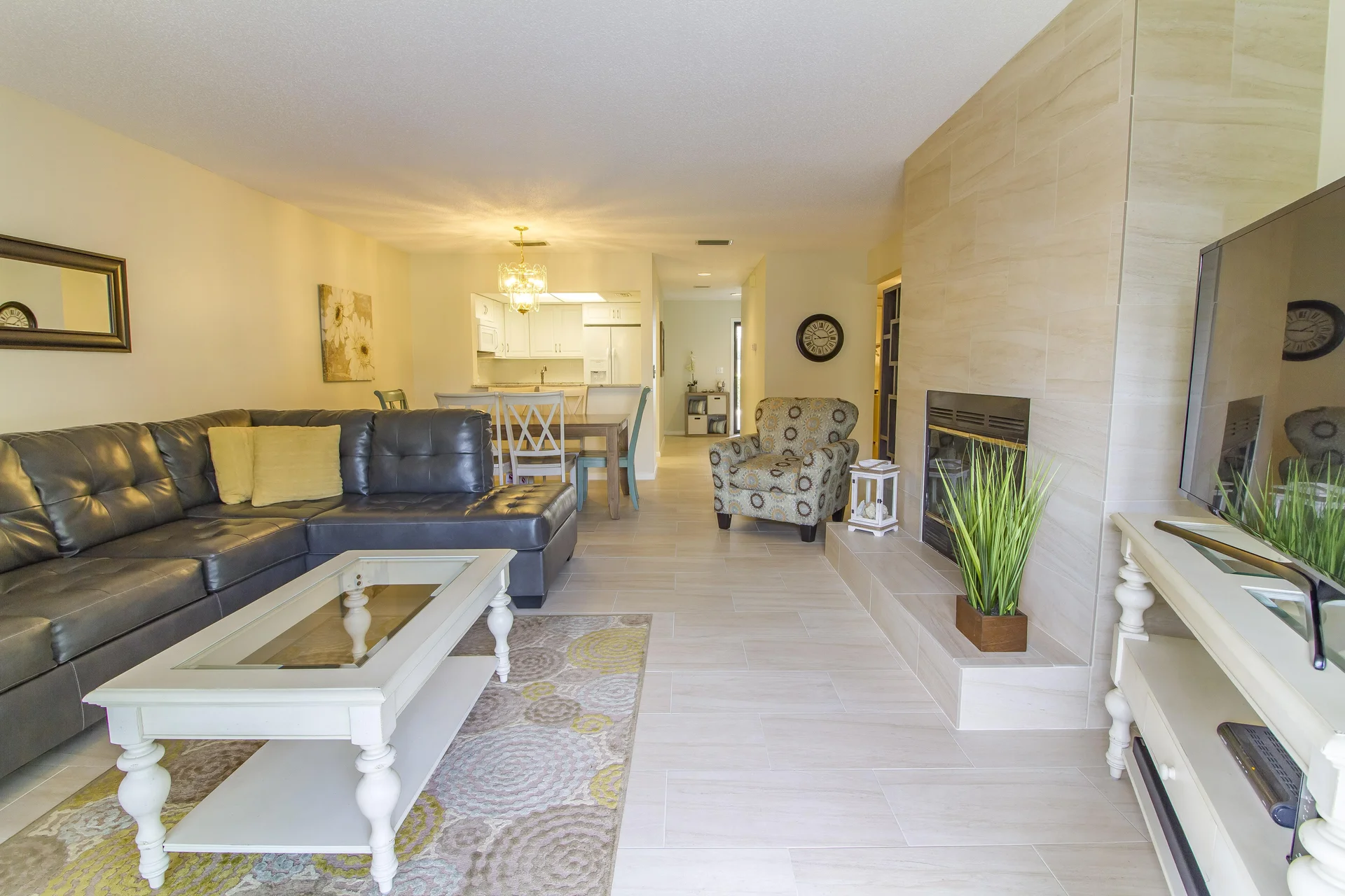 Living room with gray leather sectional, white wood coffee table, patterned armchair, and tiled fireplace wall.