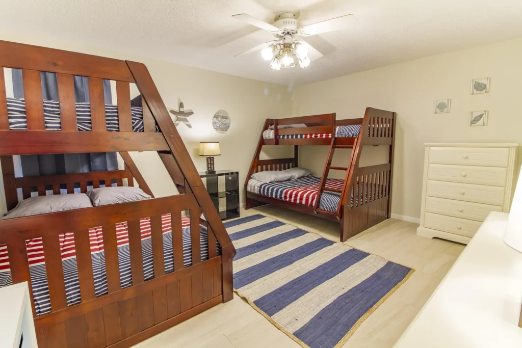 Two wooden bunk beds with navy, red, and white striped bedding sit over a blue and white striped rug.