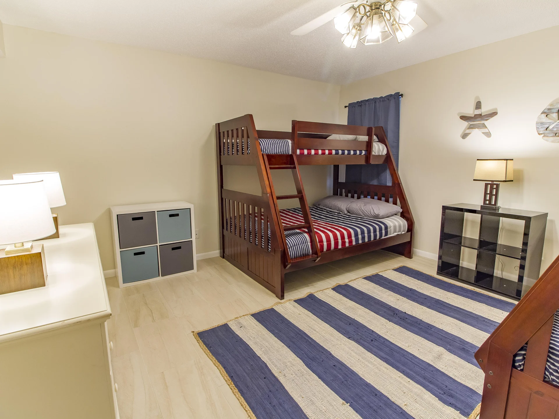 Striped blue and white area rug anchors the floor beneath a wooden bunk bed with red, white, and blue bedding.