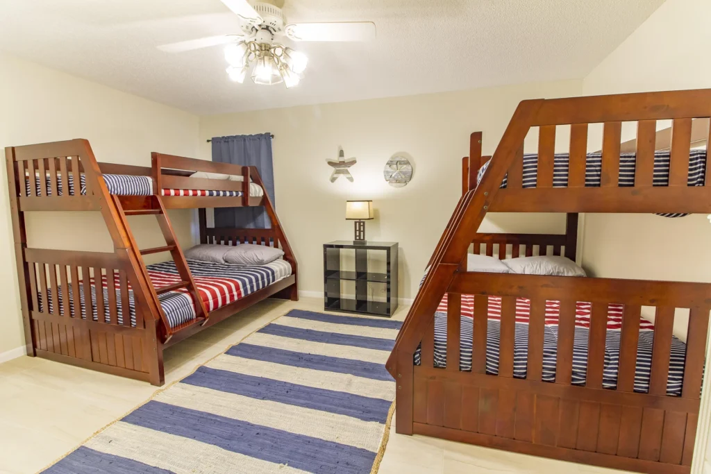 Bunk bedroom with two wooden twin-over-full beds, striped bedding, blue curtain, and a striped area rug.