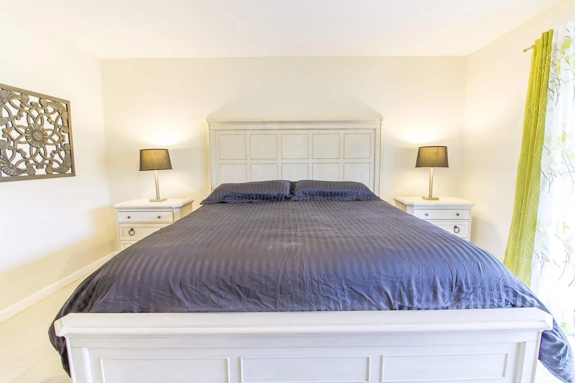 Master bedroom with white paneled bedframe, dark striped bedding, matching nightstands, and black lamps.