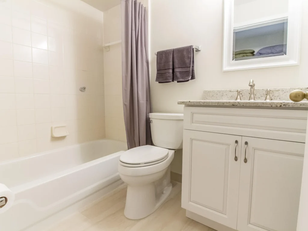 Bathroom with white tile tub and shower, gray fabric curtain, white vanity, and granite countertop.