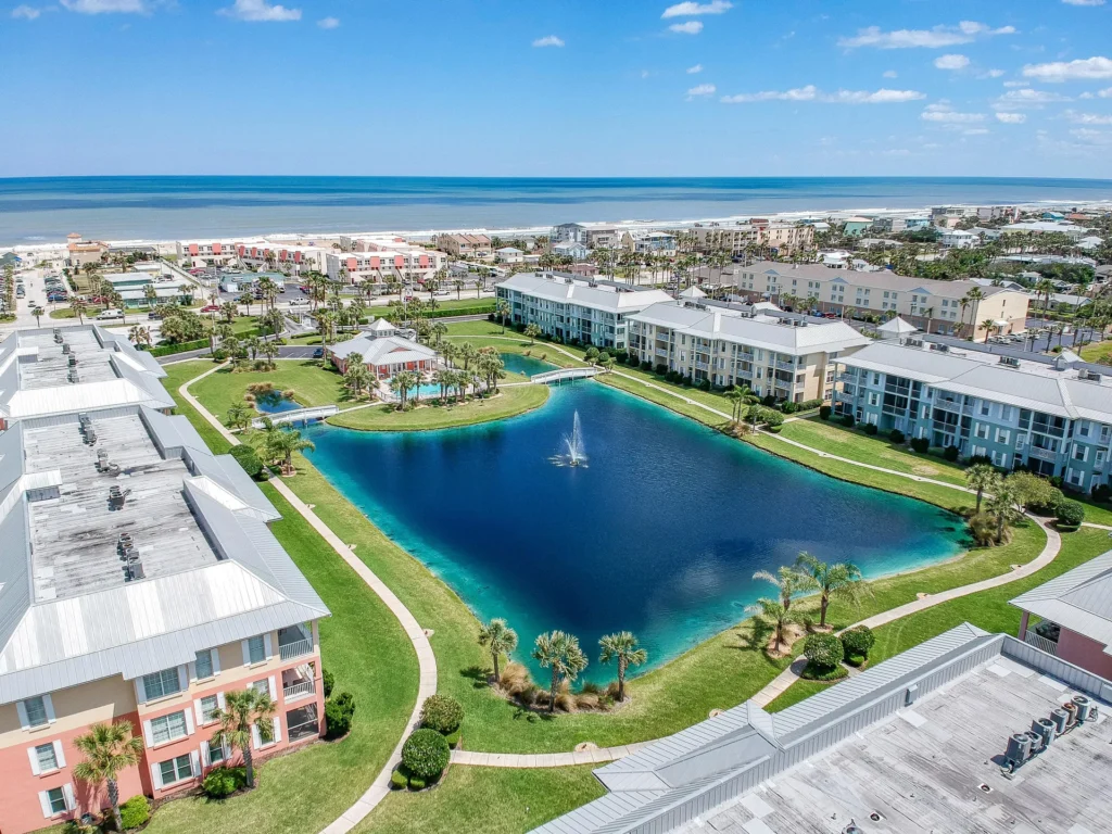 Aerial view of condo buildings surrounding a large blue pond with a central fountain and walking paths.