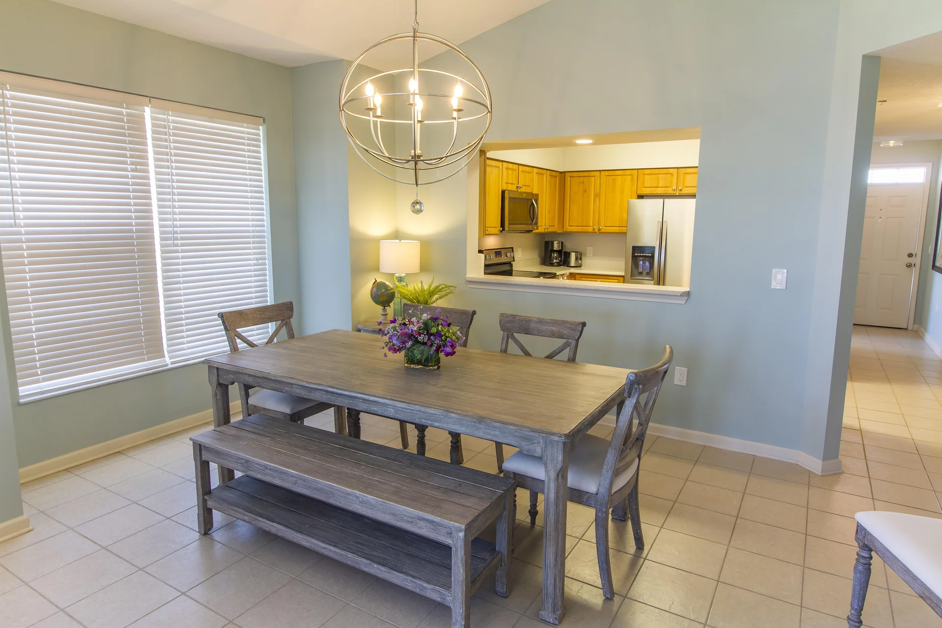 Dining area with weathered wood table, bench seating, cross-back chairs, and a spherical metal chandelier.