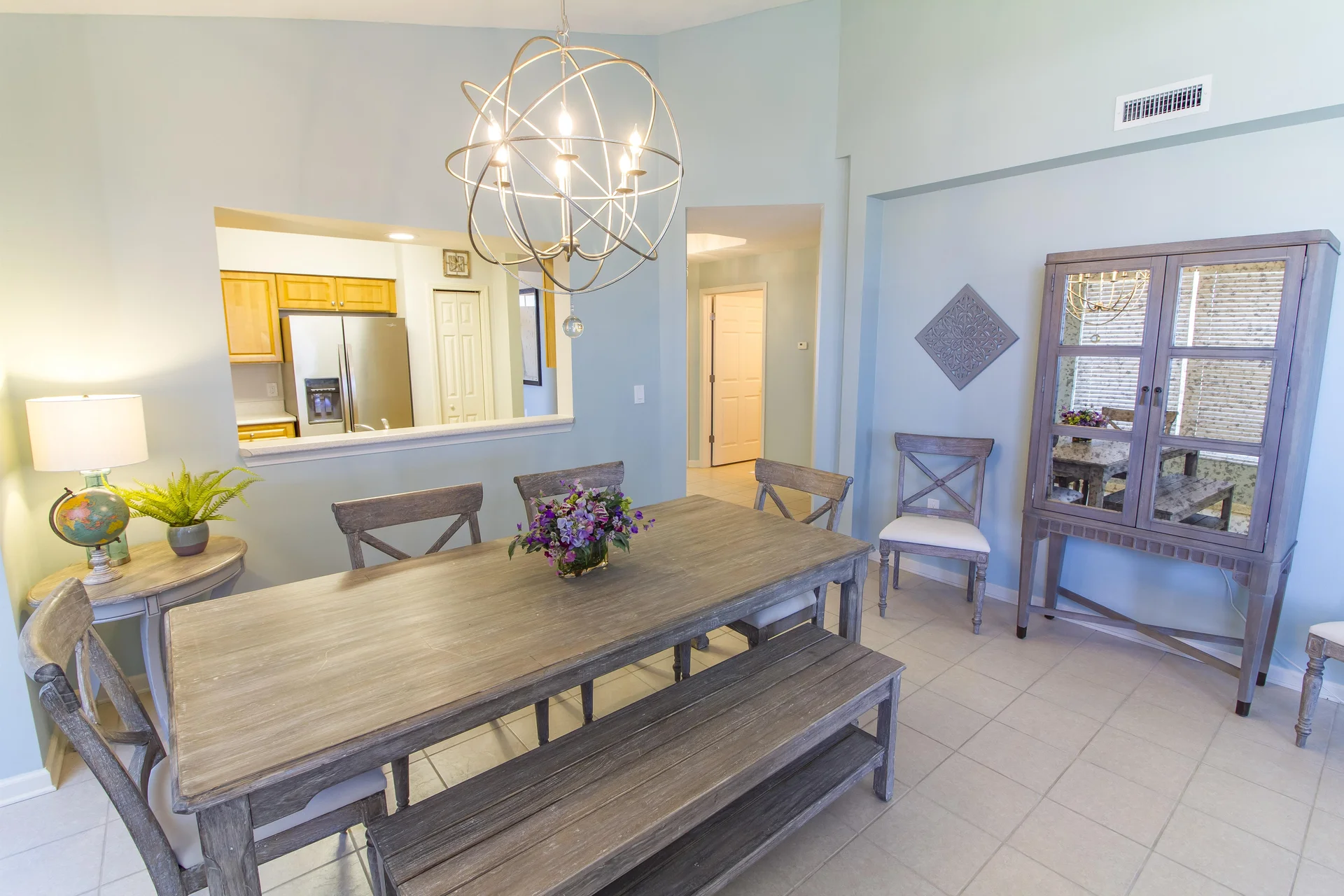 Dining room with weathered gray wood table, matching bench and chairs, and spherical metal chandelier.