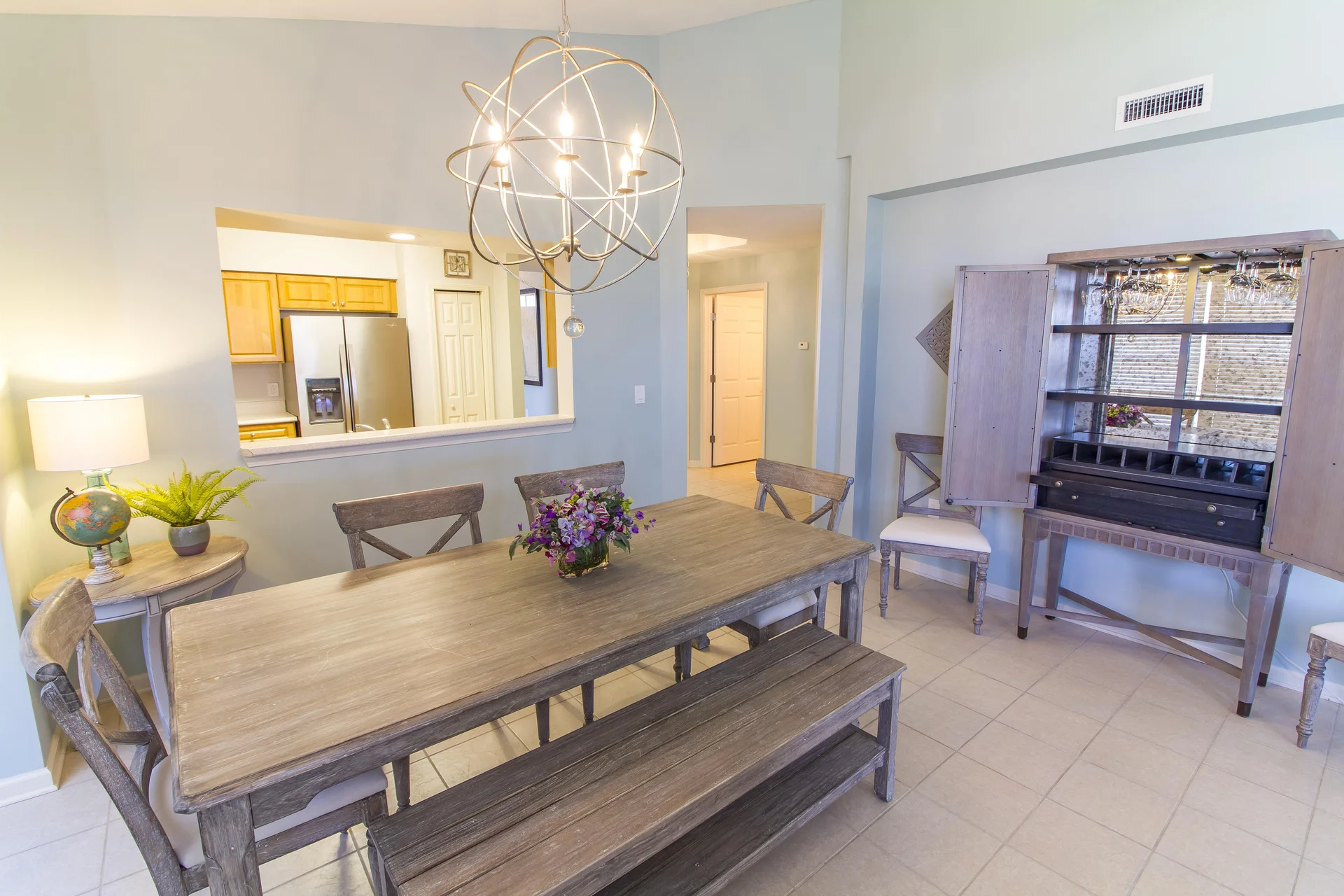 Dining room features a weathered wood table, bench, cross-back chairs, and an open cabinet with wine glasses.