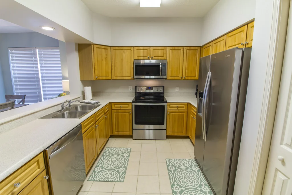 Galley kitchen with honey oak cabinets, stainless steel appliances, white quartz countertops, and patterned floor mats.