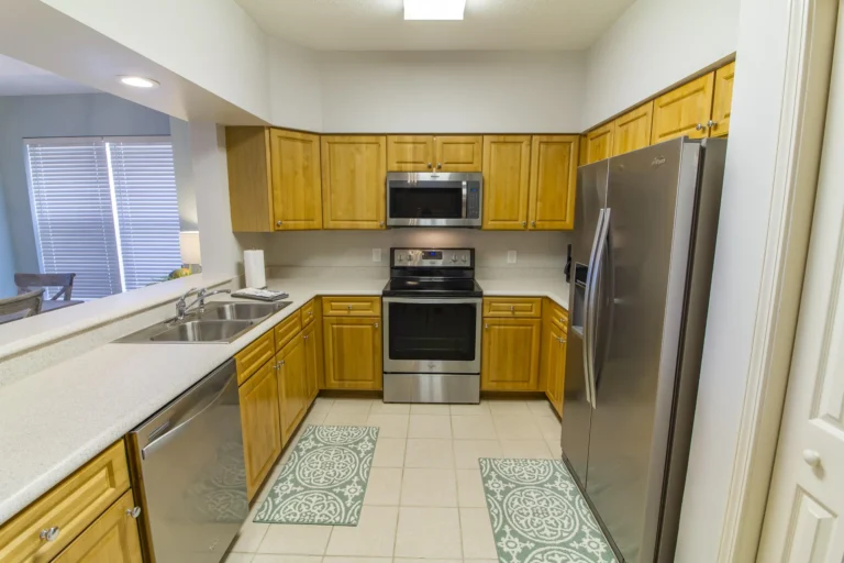 Galley kitchen with honey oak cabinets, stainless steel appliances, white quartz countertops, and patterned floor mats.