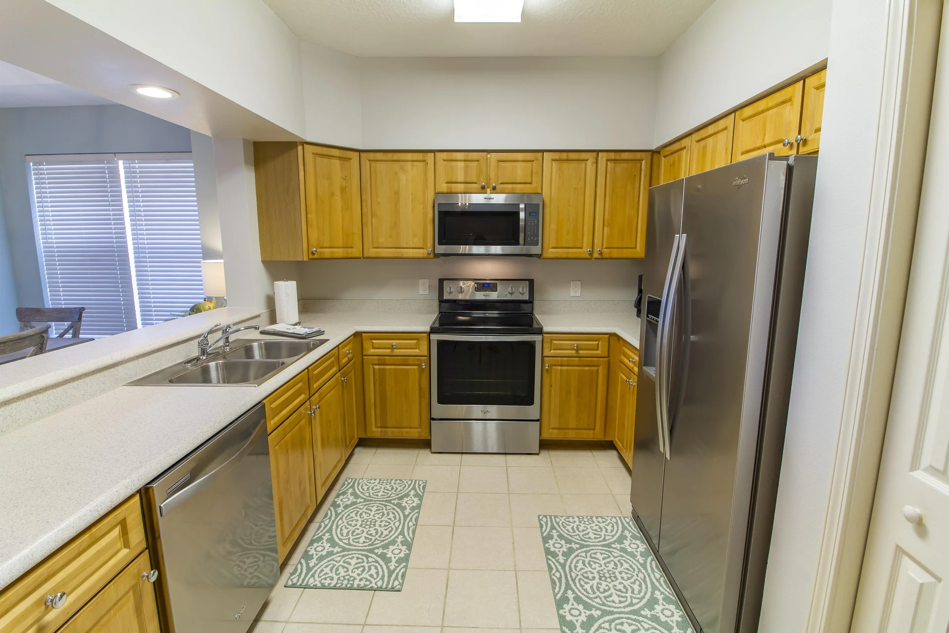 Galley kitchen with honey oak cabinets, stainless steel appliances, white quartz countertops, and patterned floor mats.