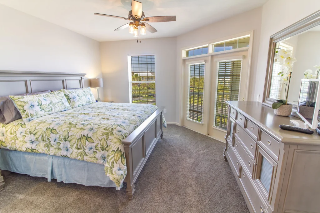 Bedroom with gray wooden bed frame, floral bedding, matching dresser, carpeted floor, and ceiling fan above.