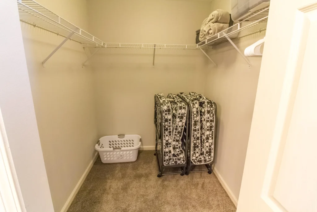 Closet with beige carpet, wire shelving along three walls, folded towels, laundry basket, and three foldable beds.