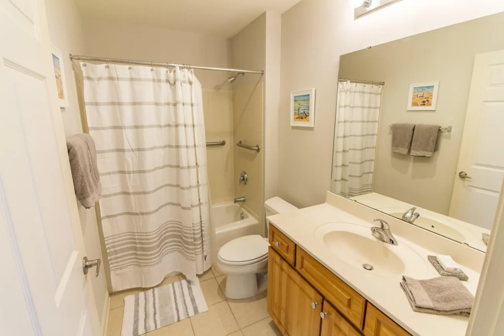 Tub and shower combination with white-striped curtain, tan tile floor, and wood vanity with single sink.