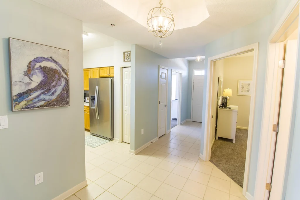 Hallway with light blue walls, white trim, tiled floor, and a modern spherical chandelier over the center.