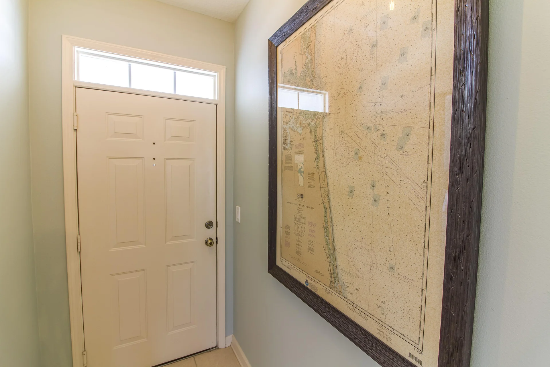 Entryway with cream paneled door, transom window above, and large framed nautical map on soft blue wall.