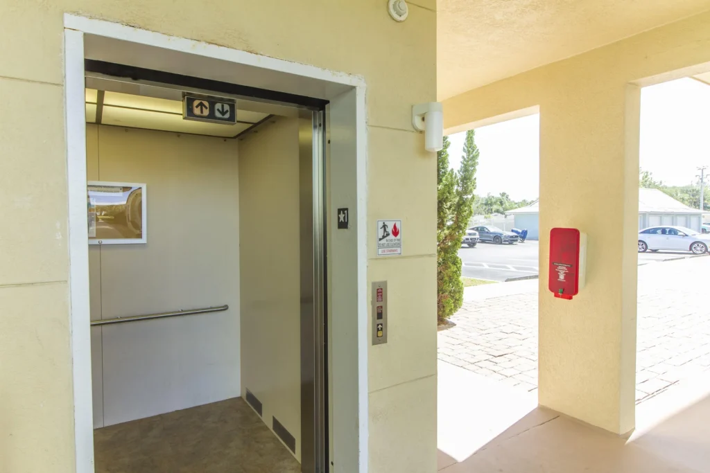Open elevator with beige walls and stainless steel trim in a covered entryway with yellow stucco walls.