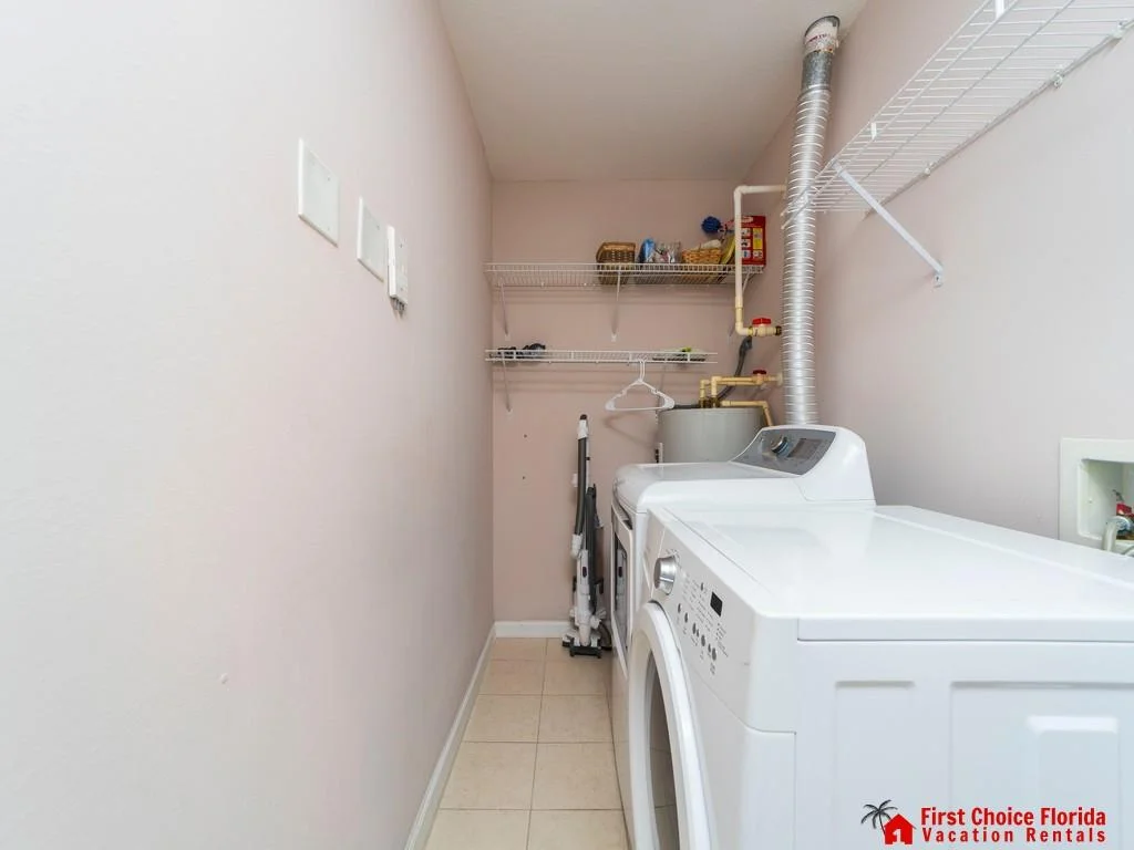 Laundry room with white washer and dryer, beige tile floor, pale pink walls, and wire shelving for storage.