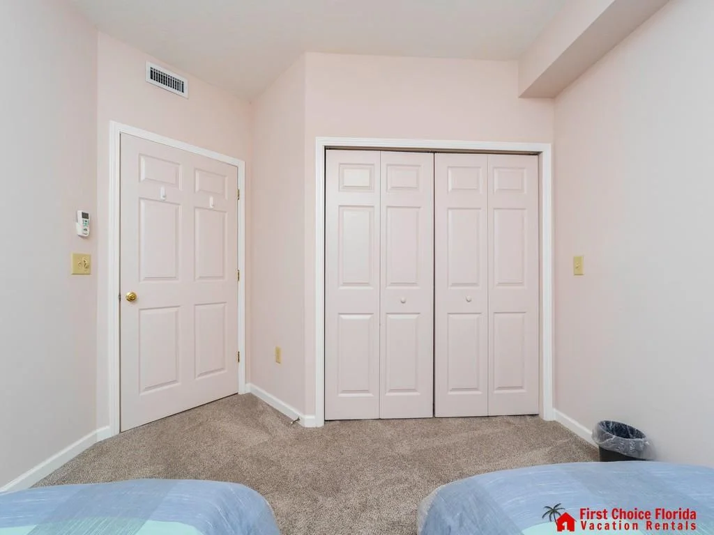 Corner of the bedroom showing beige carpet, white paneled closet doors, and a door with brass hardware.