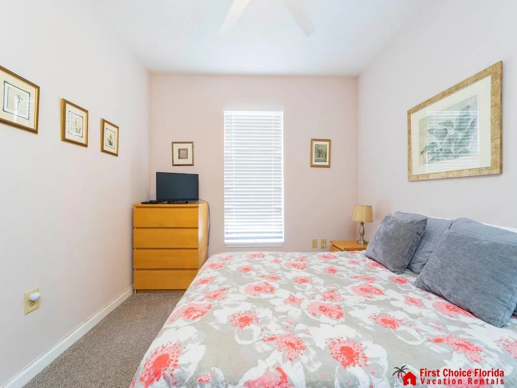 Light wood dresser topped with a small TV sits beside a window with white blinds in the bedroom.