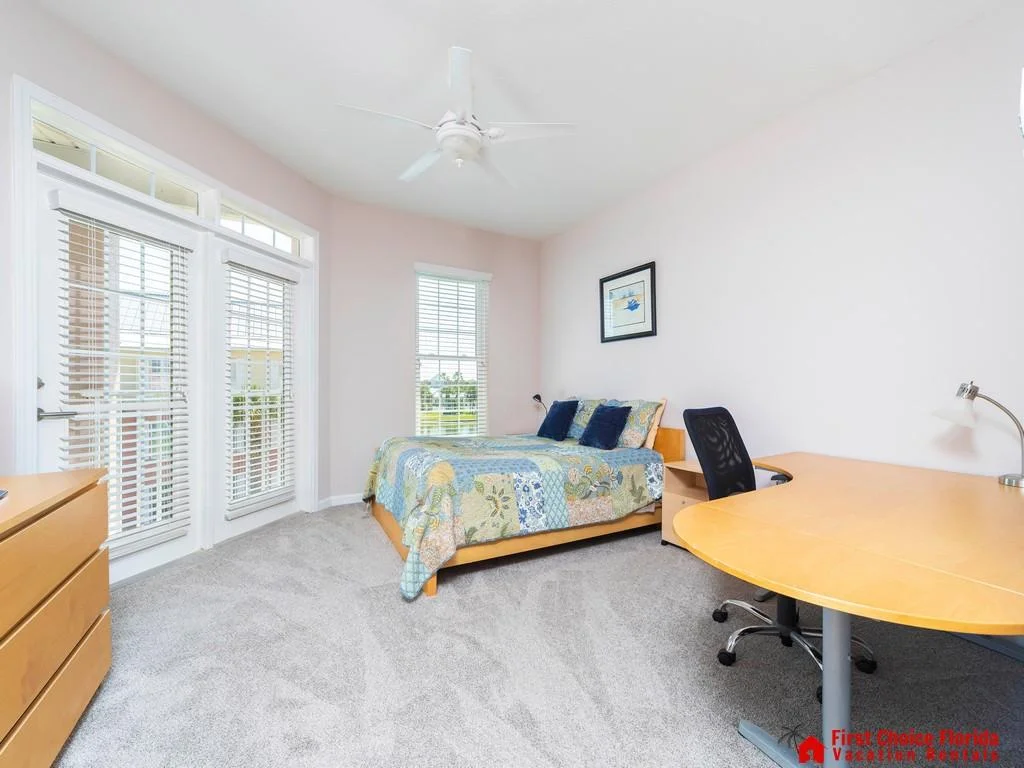 Bedroom with light wood furniture, patchwork quilt on bed, mesh office chair, and doors opening to a balcony.
