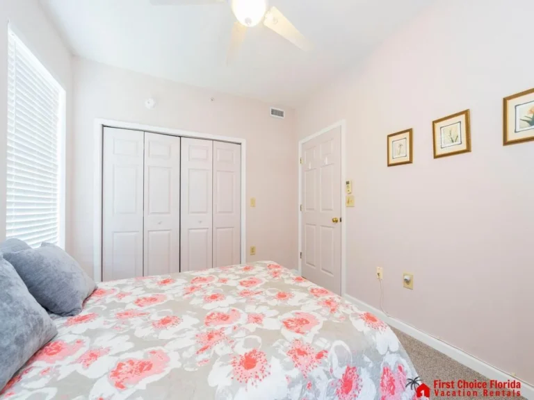 White paneled closet doors and a ceiling fan complement the bedroom’s pale pink walls and floral bedspread.