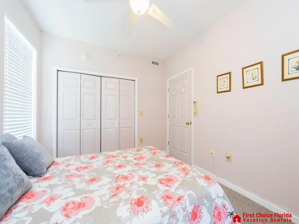 White paneled closet doors and a ceiling fan complement the bedroom’s pale pink walls and floral bedspread.